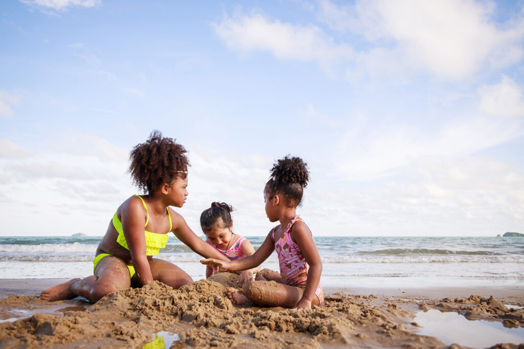 Happy friendship. Happy vacation holiday. Happy three African American kids are building a sandcastle on tropical beach and have fun together in summer. 