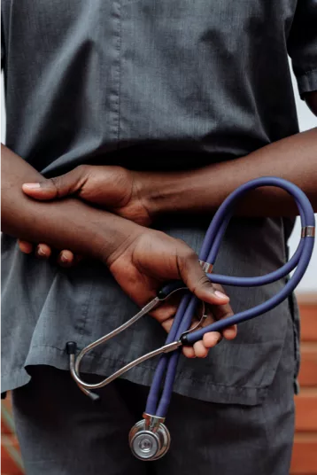 A Black nurse holding a stethoscope behind their back